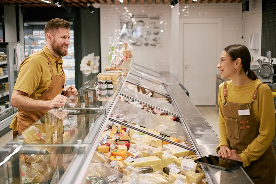Vitrina de una charcuter&iacute;a gourmet con quesos y embutidos ib&eacute;ricos perfectamente ordenados, iluminados e identificados con elegantes portaprecios.