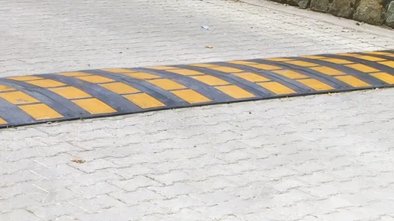 Reductores de velocidad negros y amarillos fijados con tornillos especiales en el pavimento de un parking comunitario.