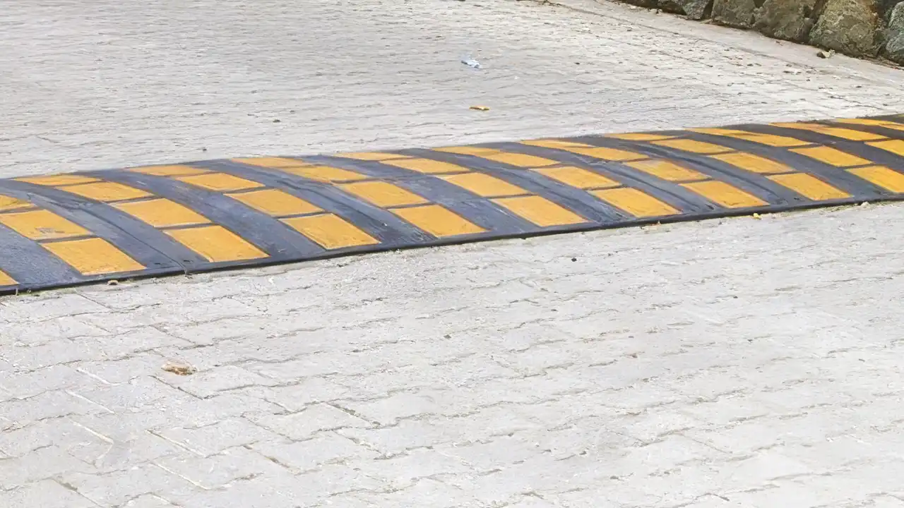 Reductores de velocidad negros y amarillos fijados con tornillos especiales en el pavimento de un parking comunitario.
