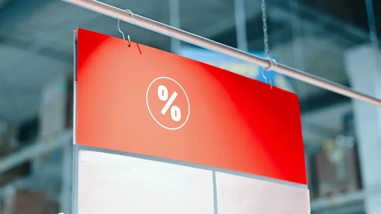 Empleado instalando carteler&iacute;a PLV promocional en el lineal de un supermercado usando ganchos r&aacute;pidos sin herramientas